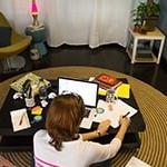 A student sits cross-legged on the floor in front of a coffee table with a laptop, 论文, 笔记本电脑, 和笔.